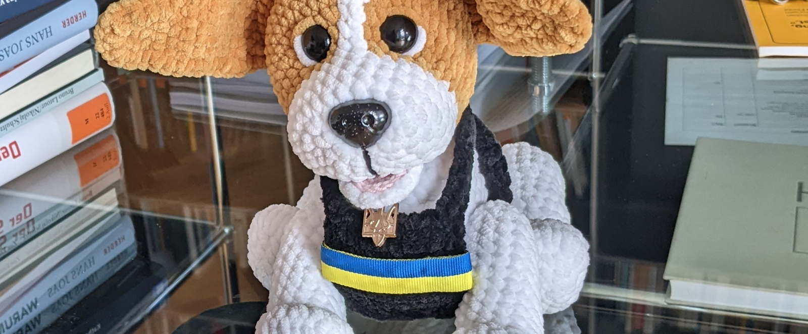 Ein Stoffhund sitzt auf einem Schreibtisch. Er trägt die Farben der Ukraine.