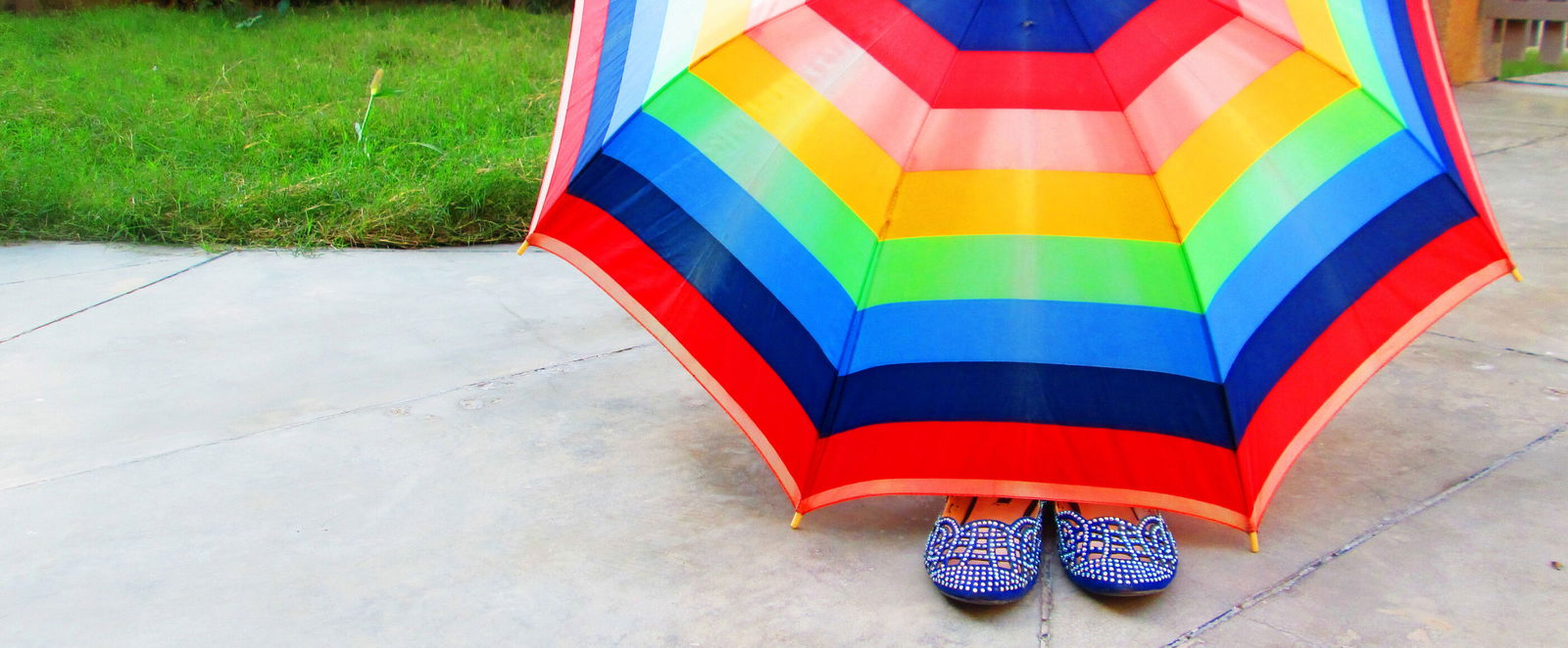 Unter einem bunten Schirm ragt ein Paar Schuhe heraus.