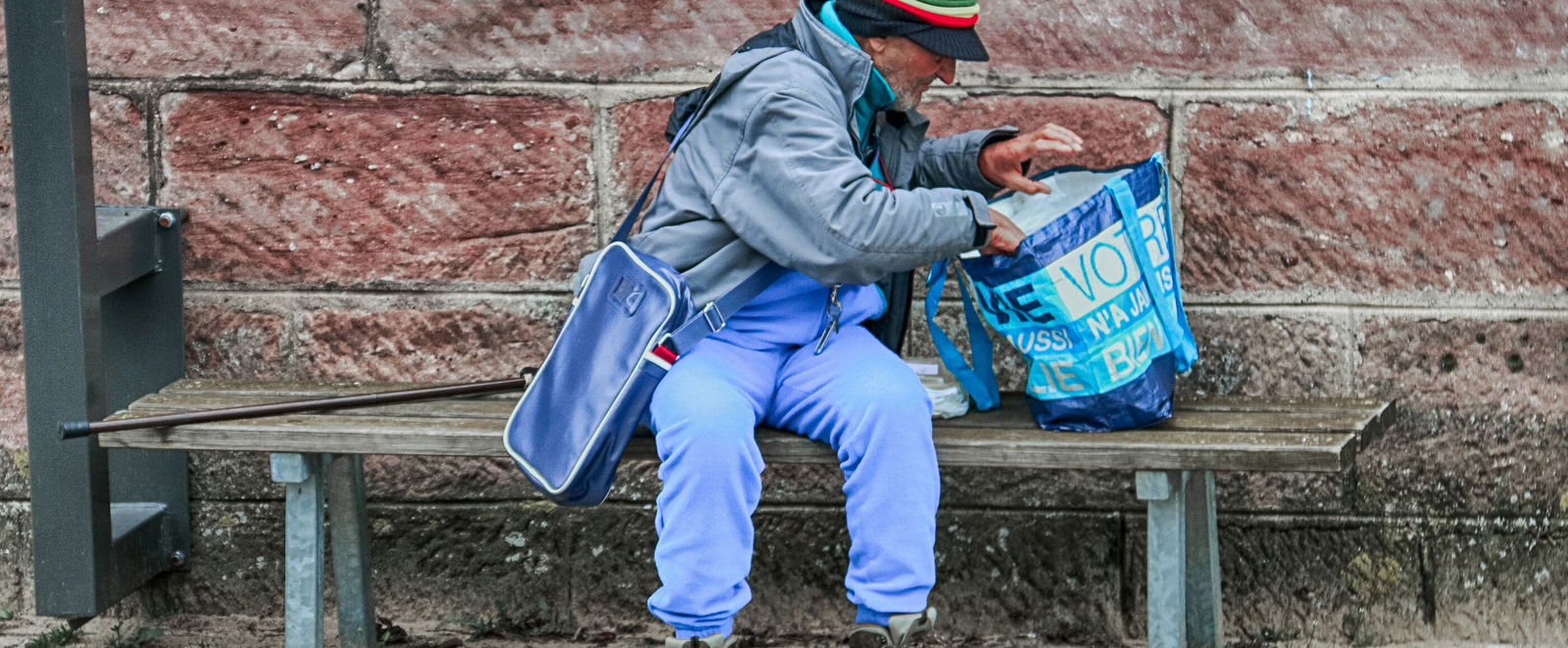 Ein älterer Mann, offenkundig wohnungslos, untersucht den Inhalt seiner Plastiktüte.