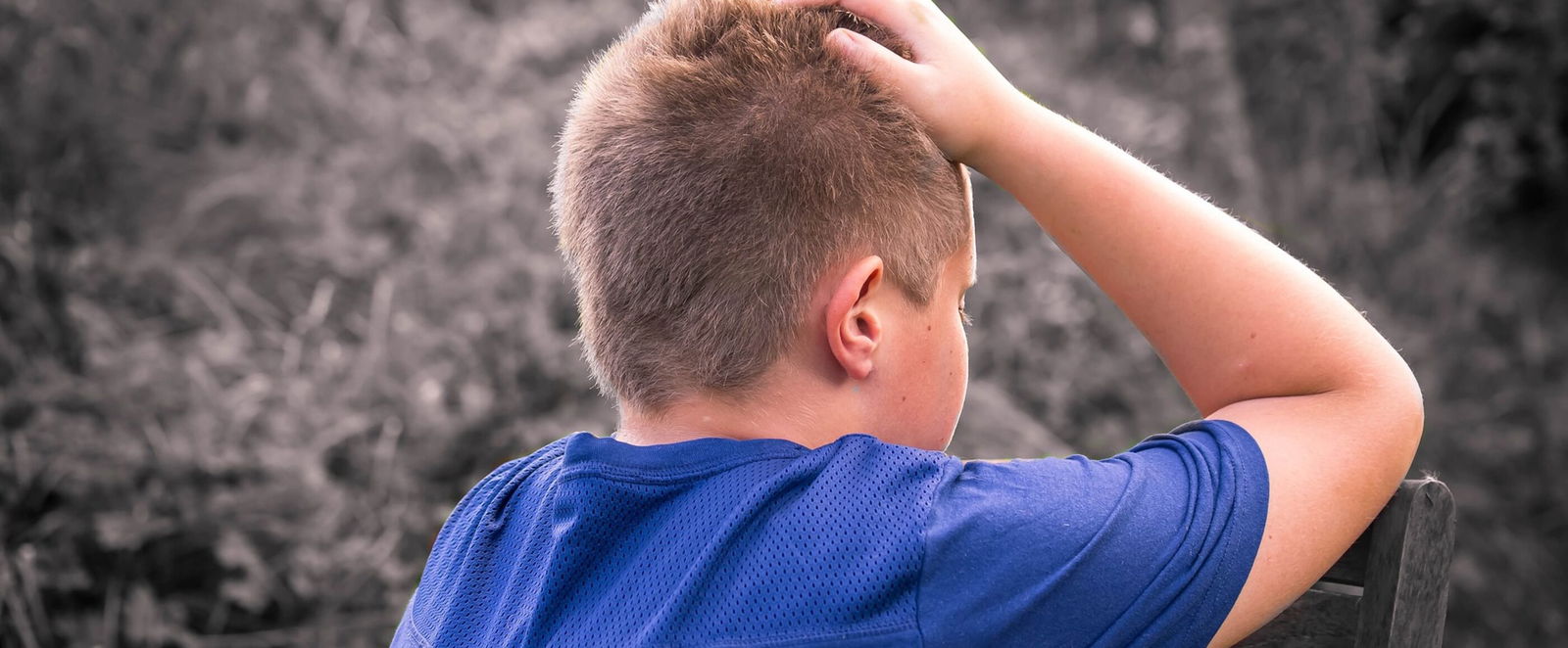 Ein Junge im blauen T-Shirt stützt an einem Baum seinen Kopf in seine Hände.