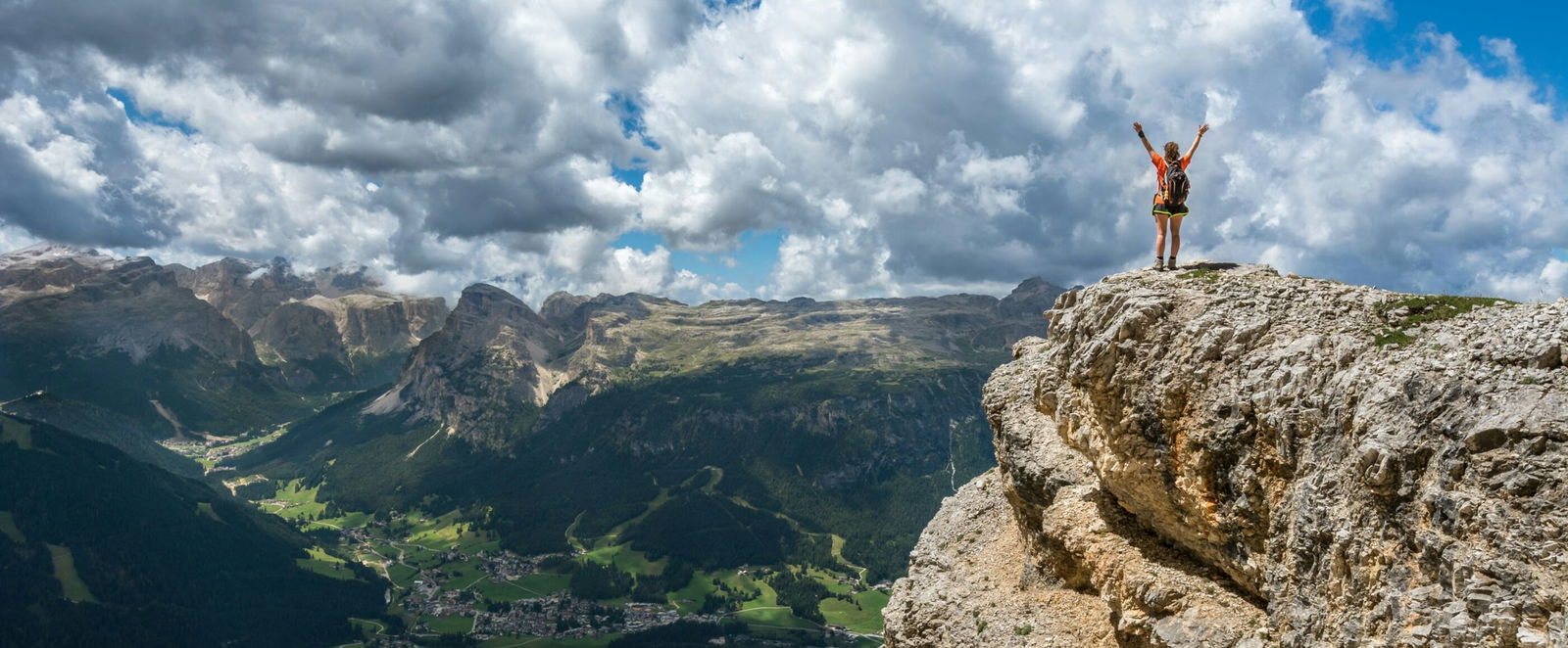 Ein Mensch mit ausgebreiteten Armen auf einem Berggipfel.