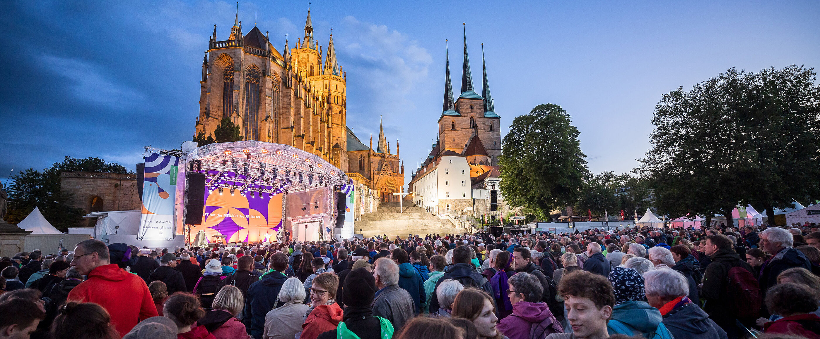 Vor zwei großen Kirchen steht eine Bühne und eine riesige Menschenmenge.