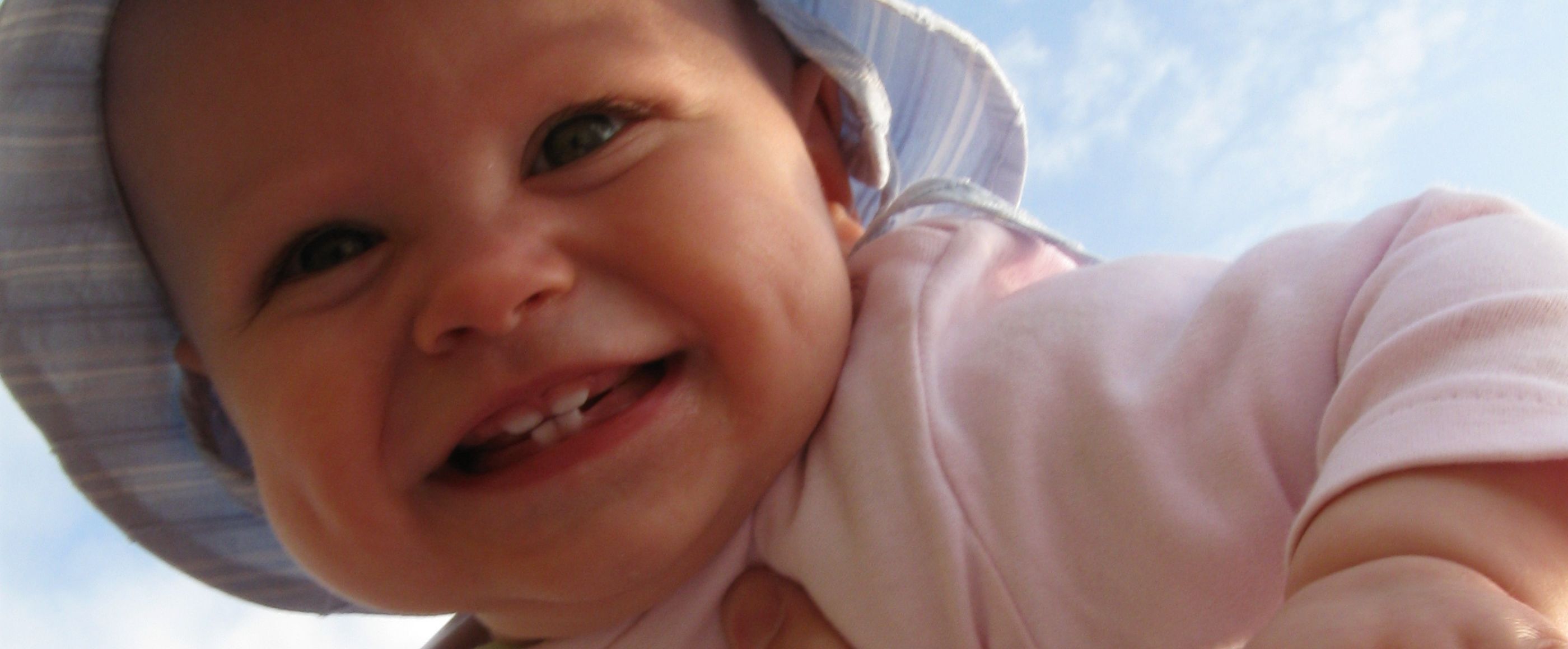 ein Baby wird von jemandem hochgehalten. Es lacht vor Freude