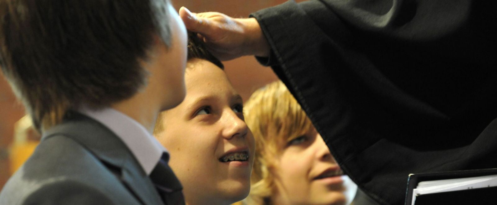 Drei als Jungs lesbare Personen blicken zu einem Pastor auf, der einem von ihnen die Hand auflegt