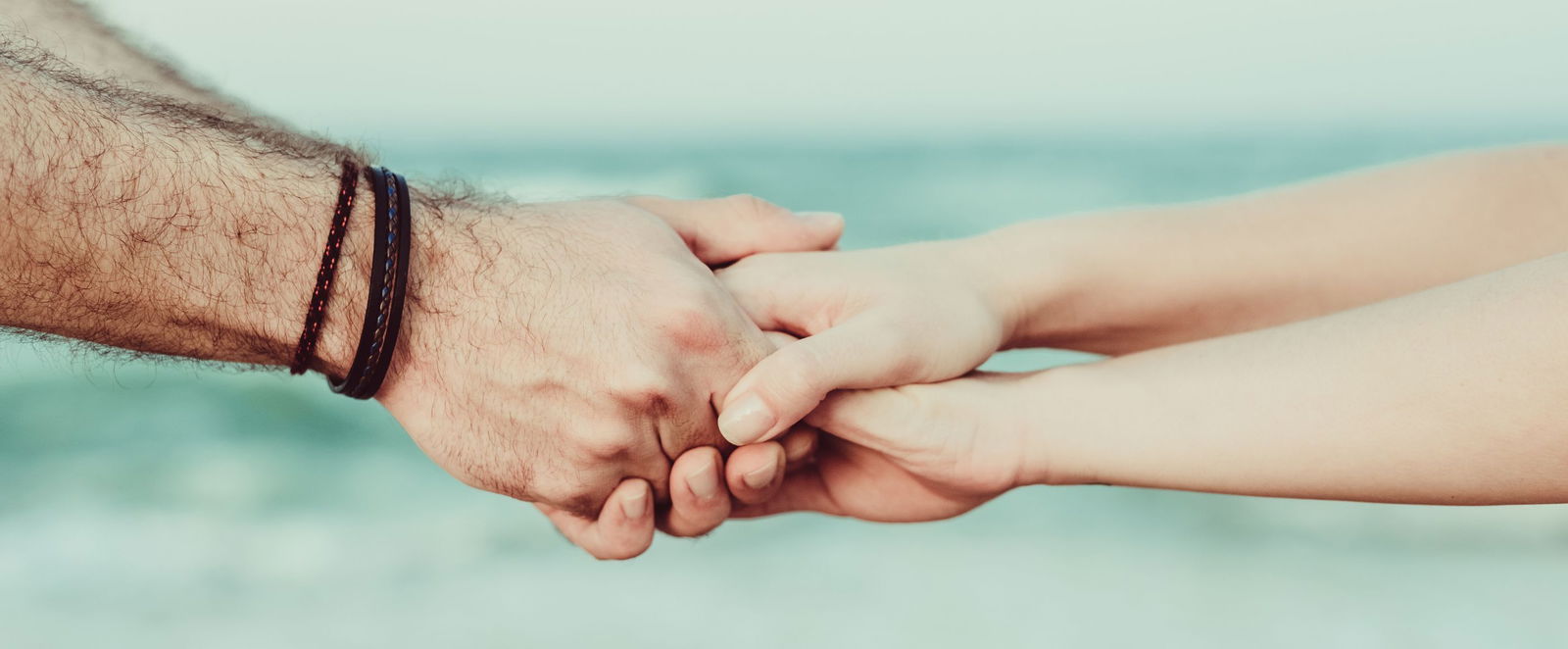 zwei Menschen reichen sich an einem Strand die Haende