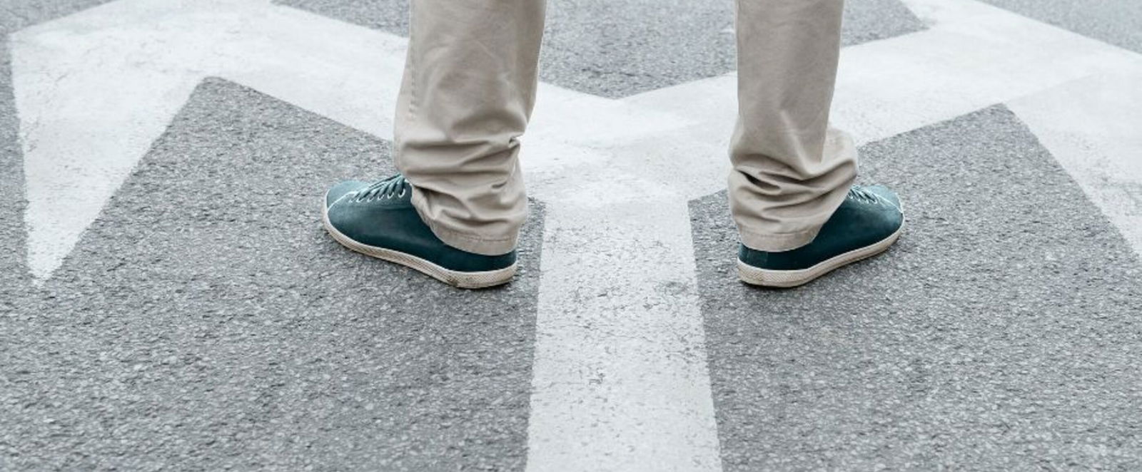 Eine Person mit grauer Hose steht auf einem weißen Pfeil auf der Straße. Der Pfeil teilt sich: nach links und rechts.