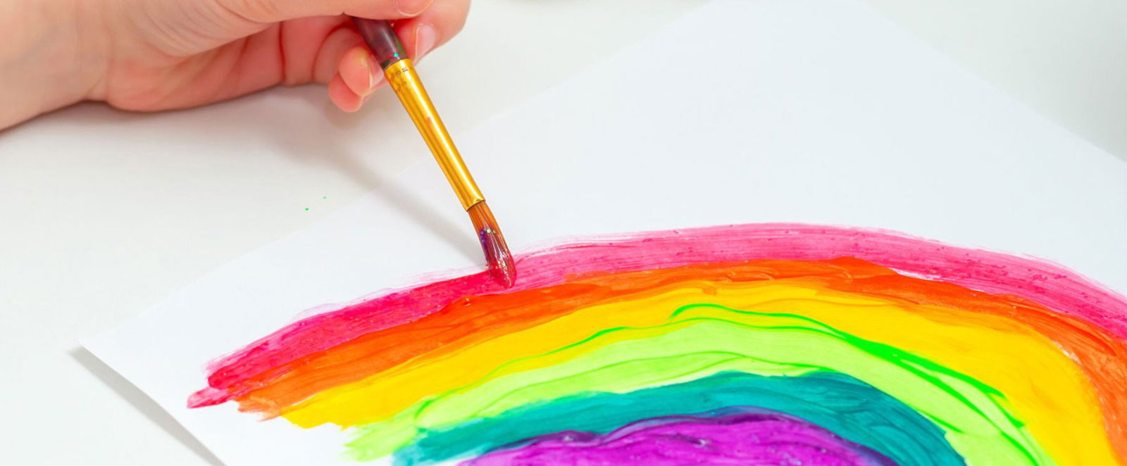 Eine Hand malt mit Tusche einen Regenbogen.