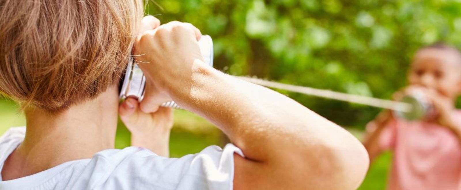 Zwei Kinder spielen mit einem Dosentelefon im Grünen.