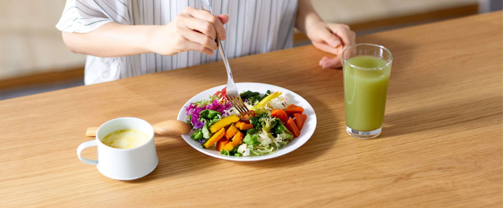 Eine Person sitzt an einem Tisch vor einem gesunden veganen Essen, einem Gemüse-Smoothie und einem Kaffee.