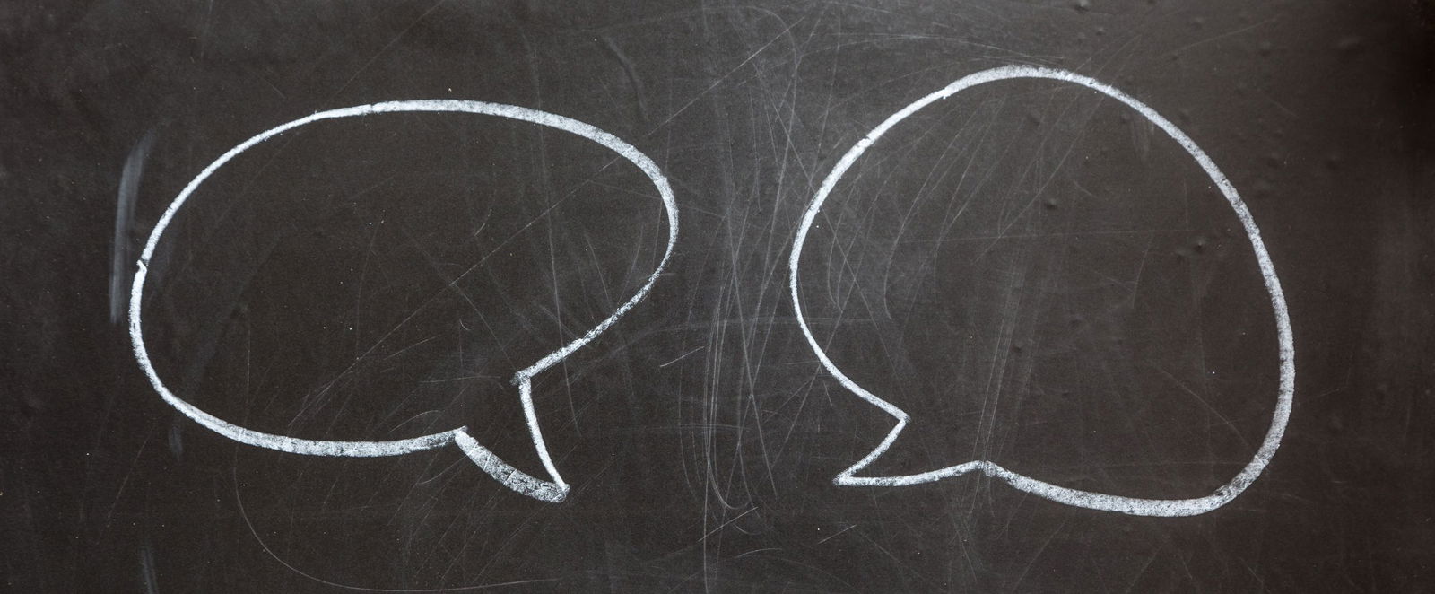 Auf einer Tafel sind mit weißer Kreide zwei Sprechblasen zu sehen.