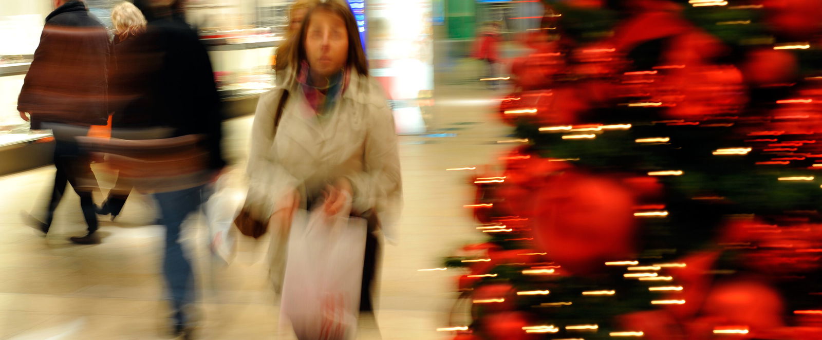 Eine als Frau lesbare Person geht an einem geschmückten Weihnachtsbaum vorbei.