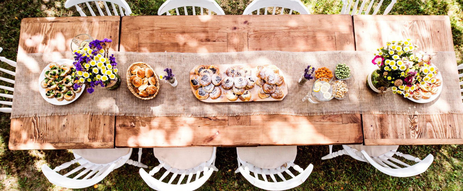 Eine langer gedeckter Tisch im Garten mit weißen Stühlen