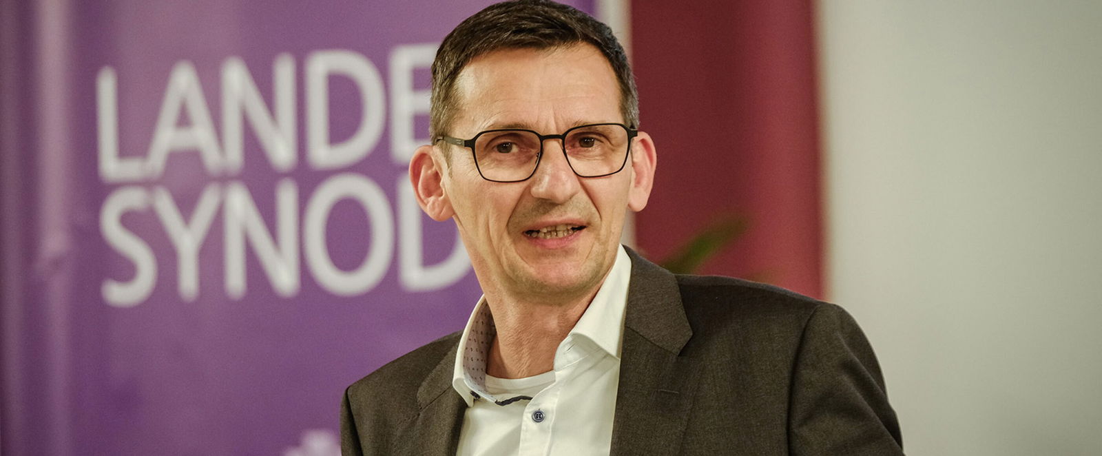 Eine männlich gelesene Person mit dunklen, kurzen Haaren und Brille. 