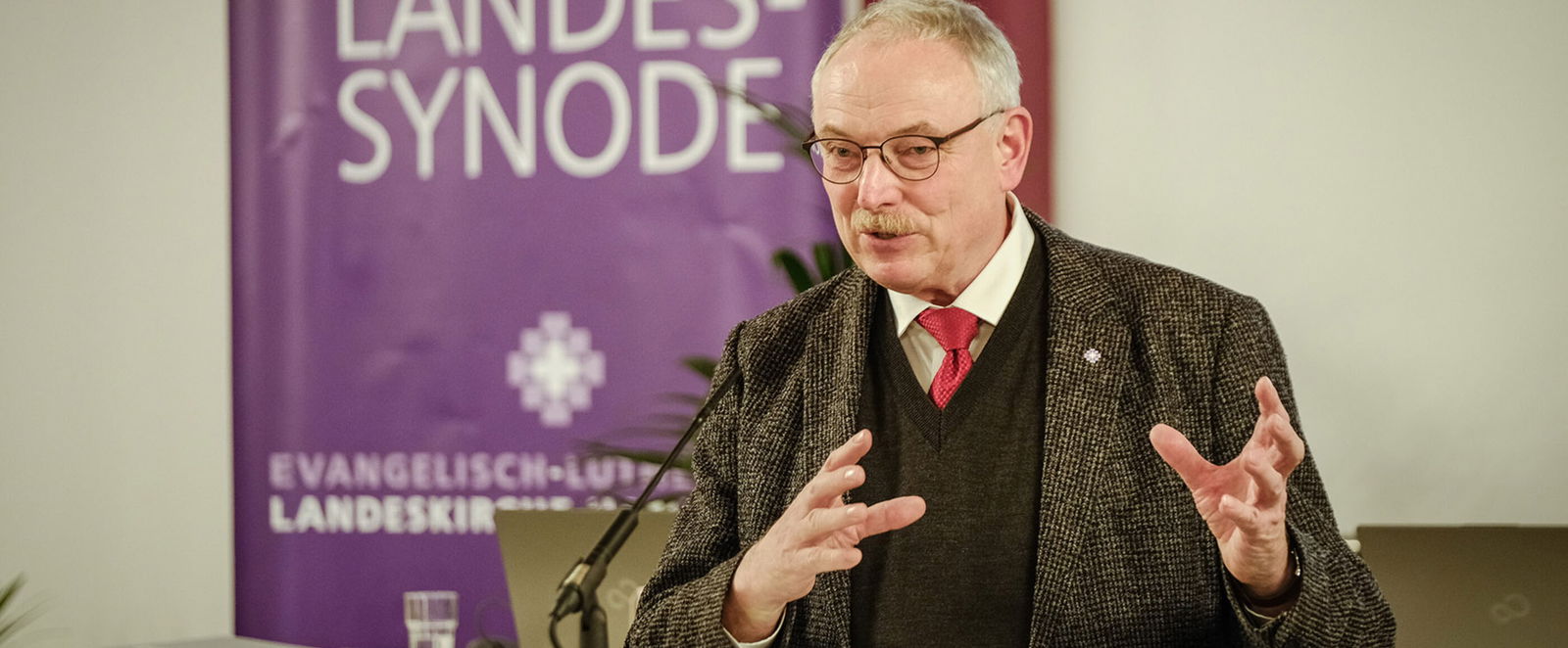 Eine männlich gelesene Person mit kurzen grauen Haaren am Redepult. 