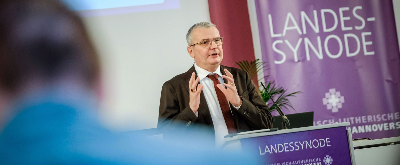 Eine männlich lesbare Person an einem Rednerpult