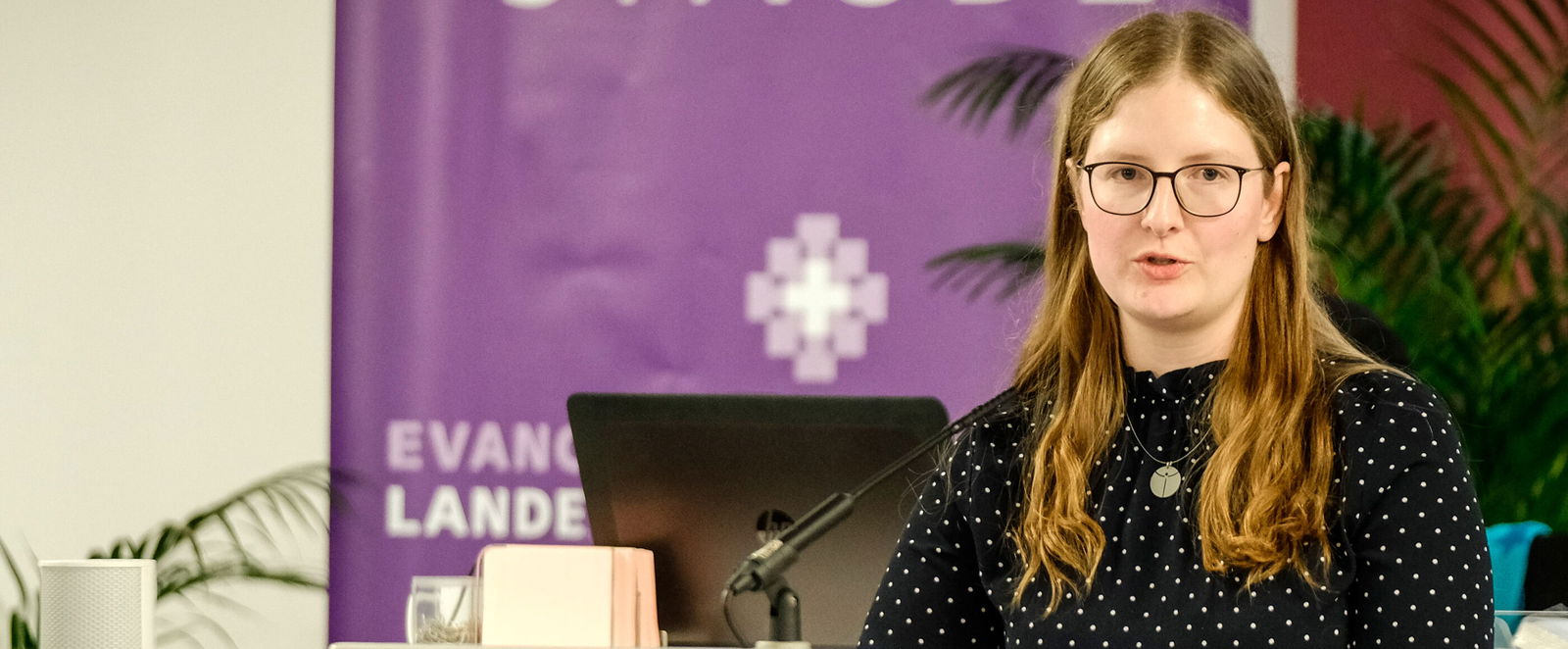 Eine weiblich lesbare Person steht am Podium und spricht.