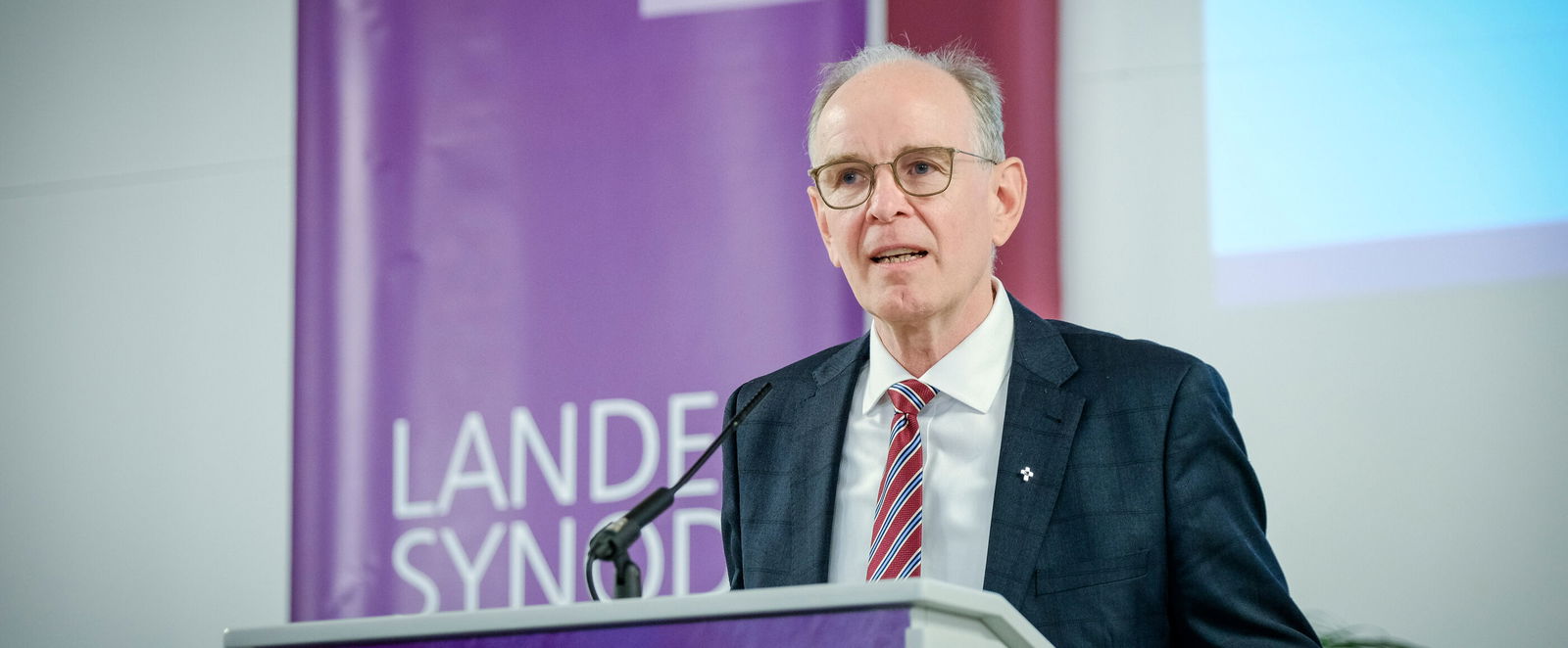 Eine männlich lesbare Person im Anzug steht am Podium