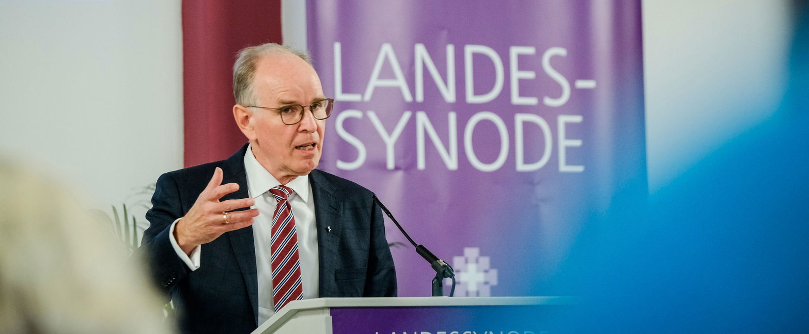 Eine männlich lesbare Person im Anzug steht am Podium