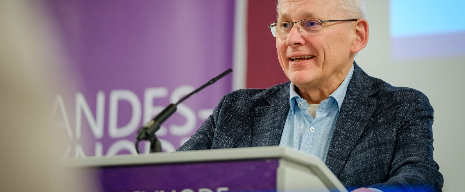 Eine männlich lesbare Person steht am Rednerpult und spricht.