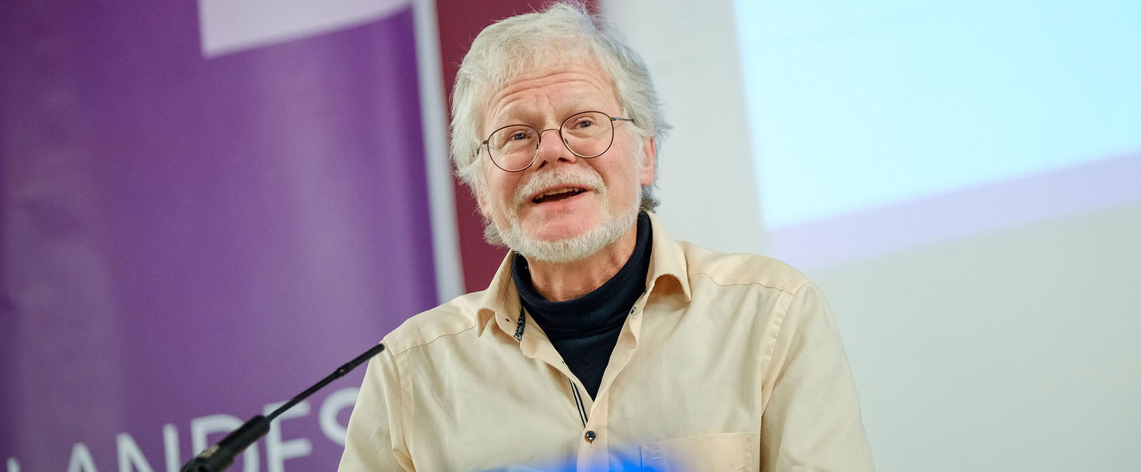 Eine männlich lesbare Person steht am Rednerpult und spricht