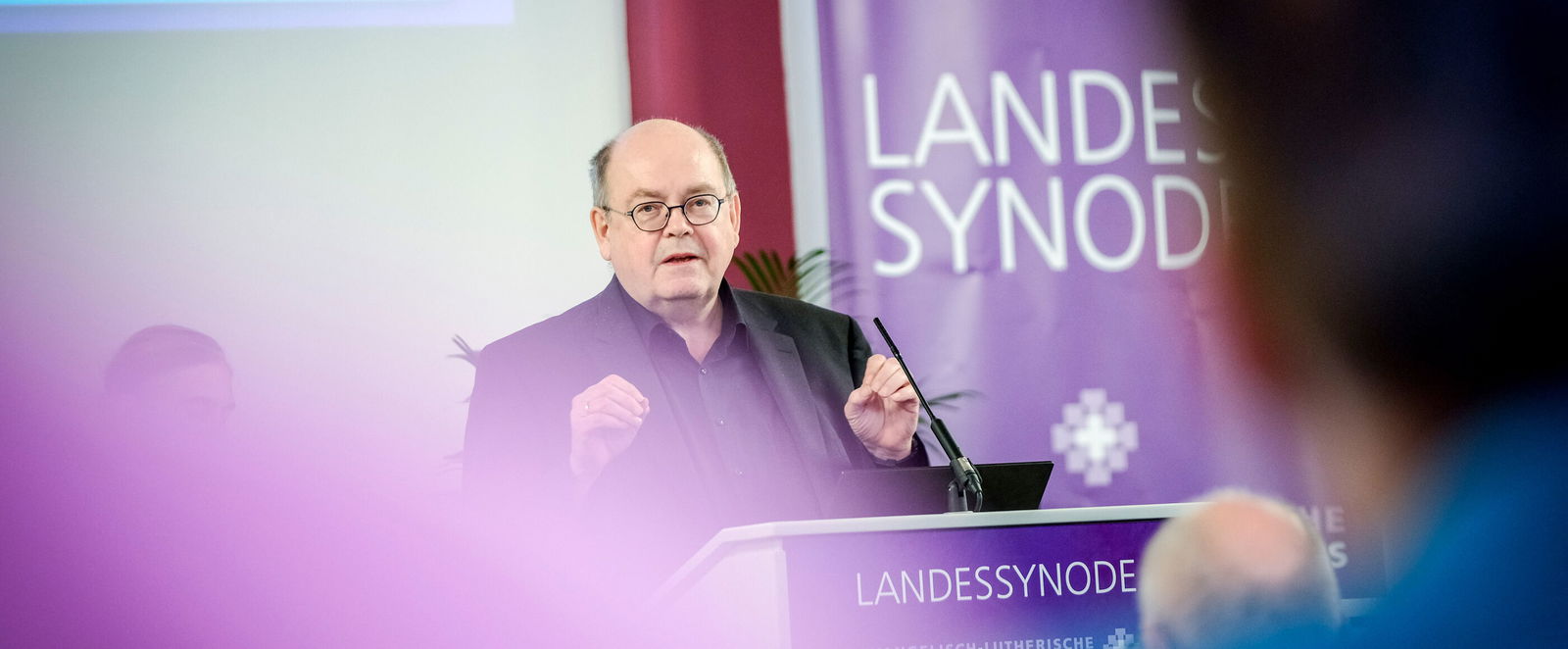 Eine männlich lesbare Person an einem Rednerpult