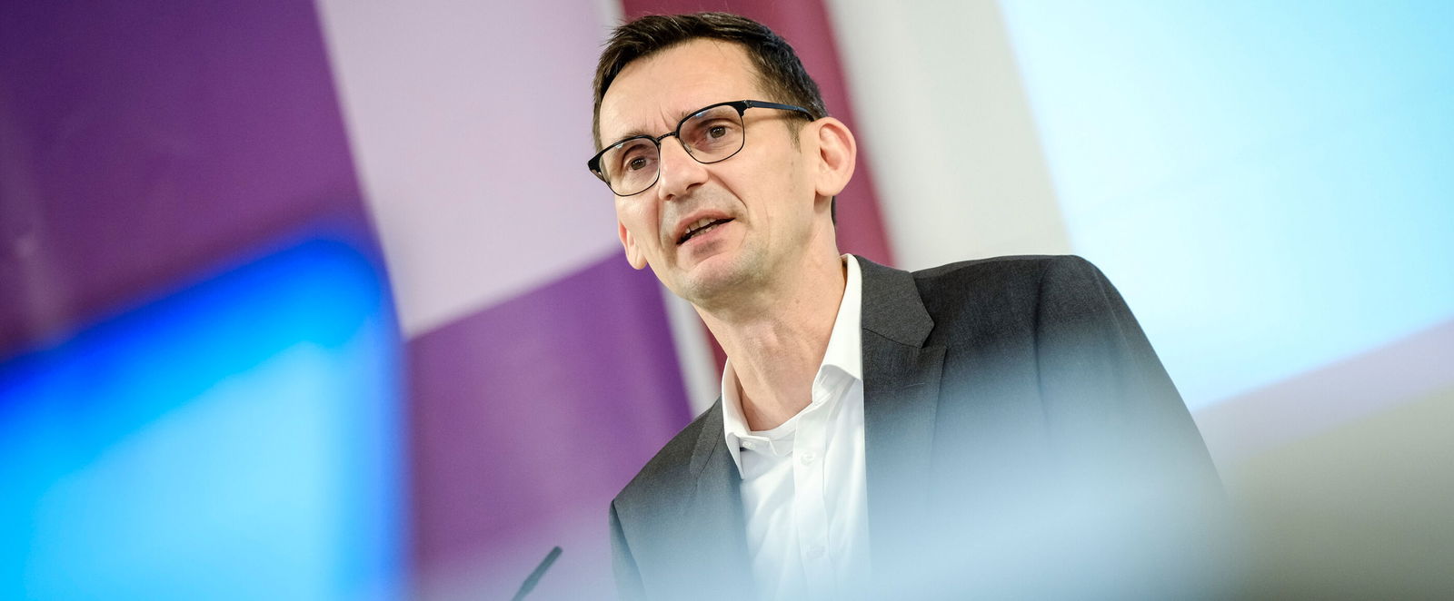 Eine männlich gelesene Person mit Brille und kurzen Haaren am Podium.