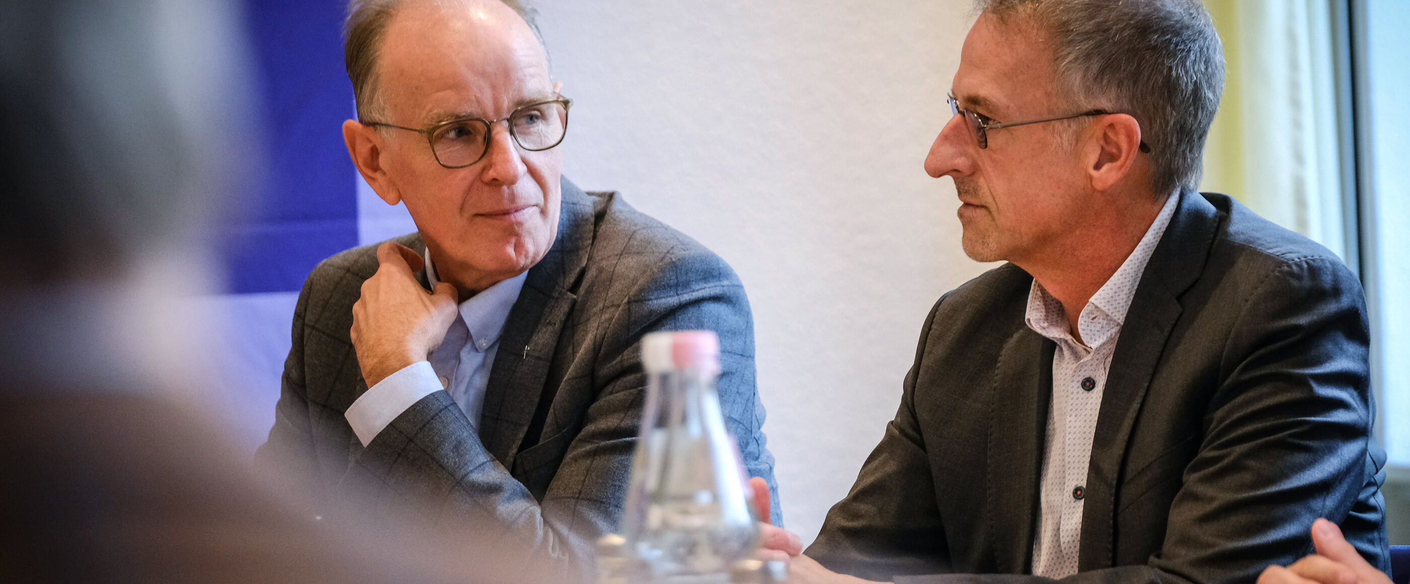 Zweie männlich lesbare Personen an einem Tisch im Gespräch
