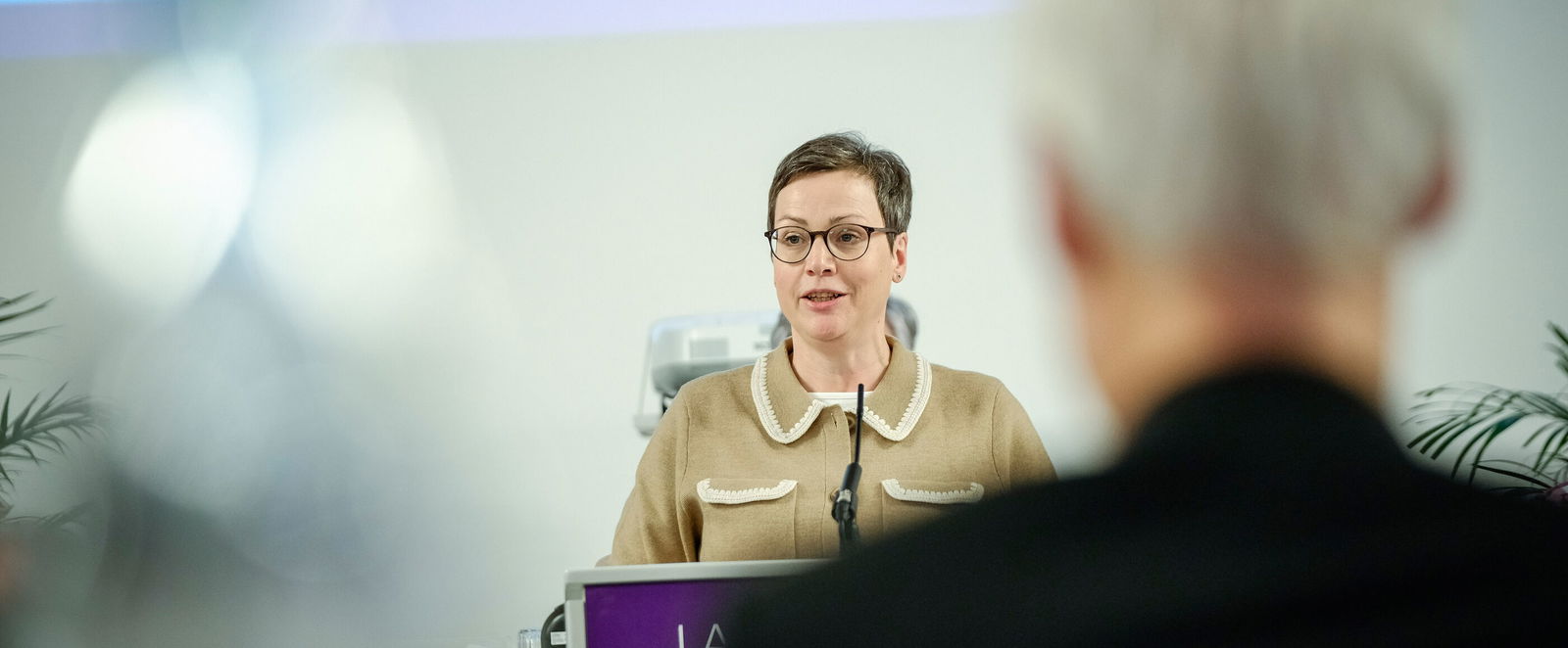 Eine weiblich lesbare Person steht am Podium und spricht.