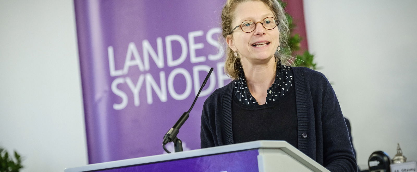 Eine weiblich lesbare Person steht an einem Rednerpult und spricht