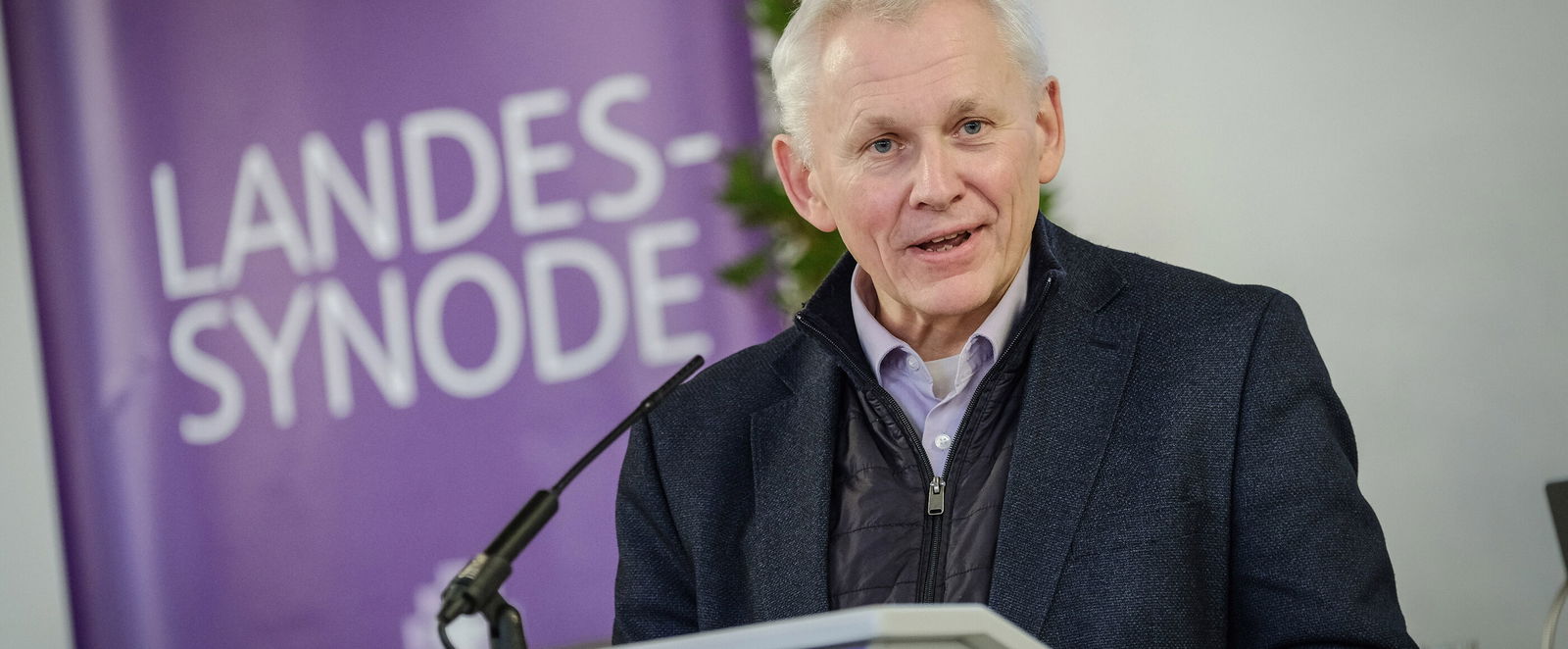 Eine männlich lesbare Person steht an einem Rednerpult und spricht