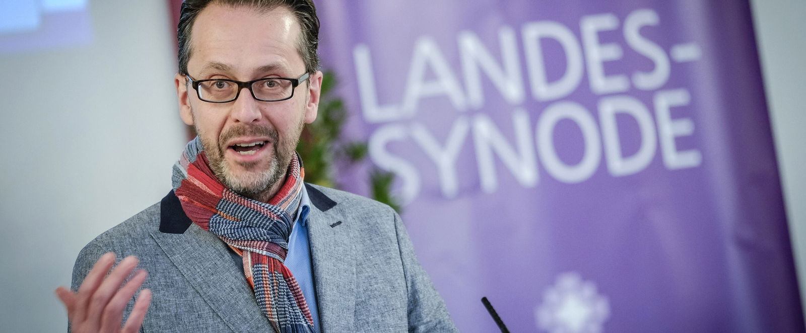 Eine männlich lesbare Person steht an einem Rednerpult