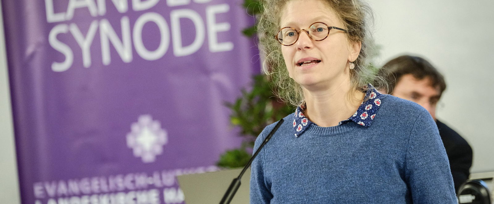 Eine weiblich lesbare Person steht an einem Rednerpult