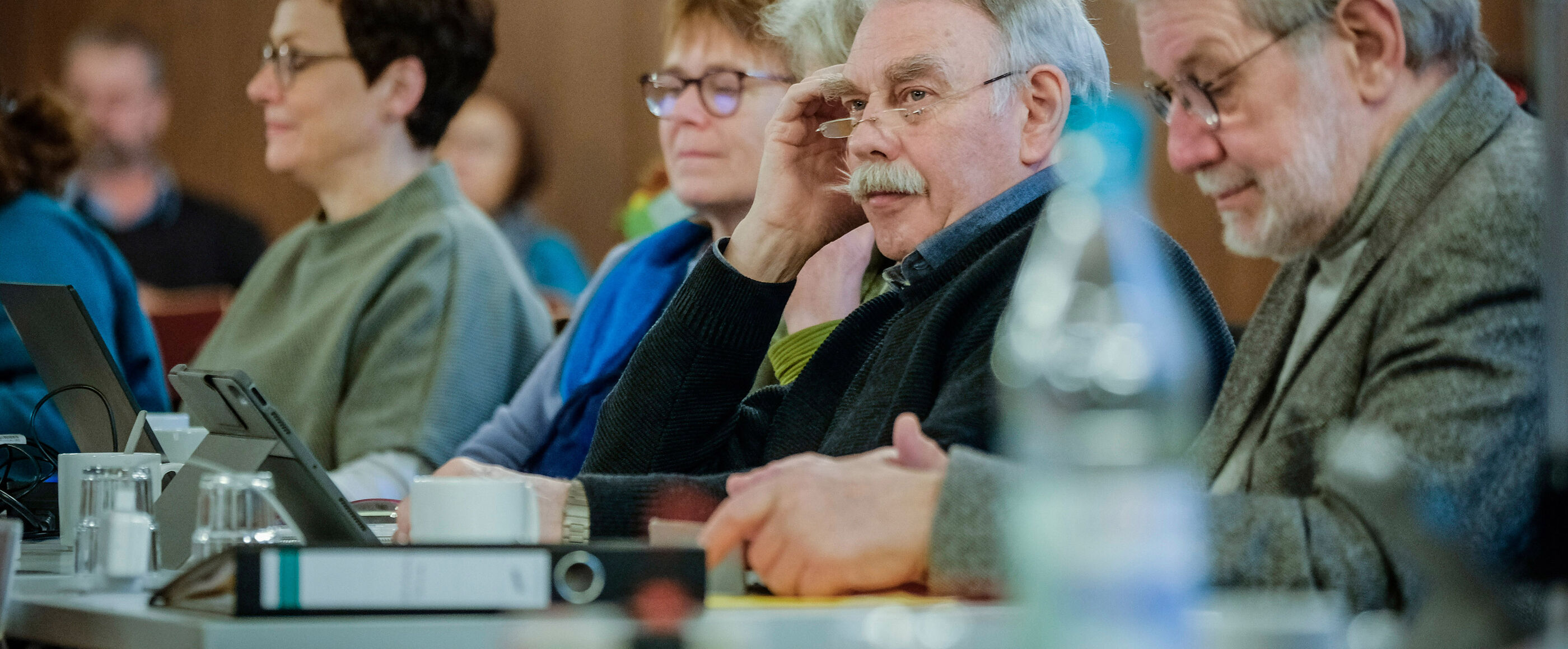 Eine Gruppe von Personen sitzt an einem langen Tisch und hört jemandem zu.
