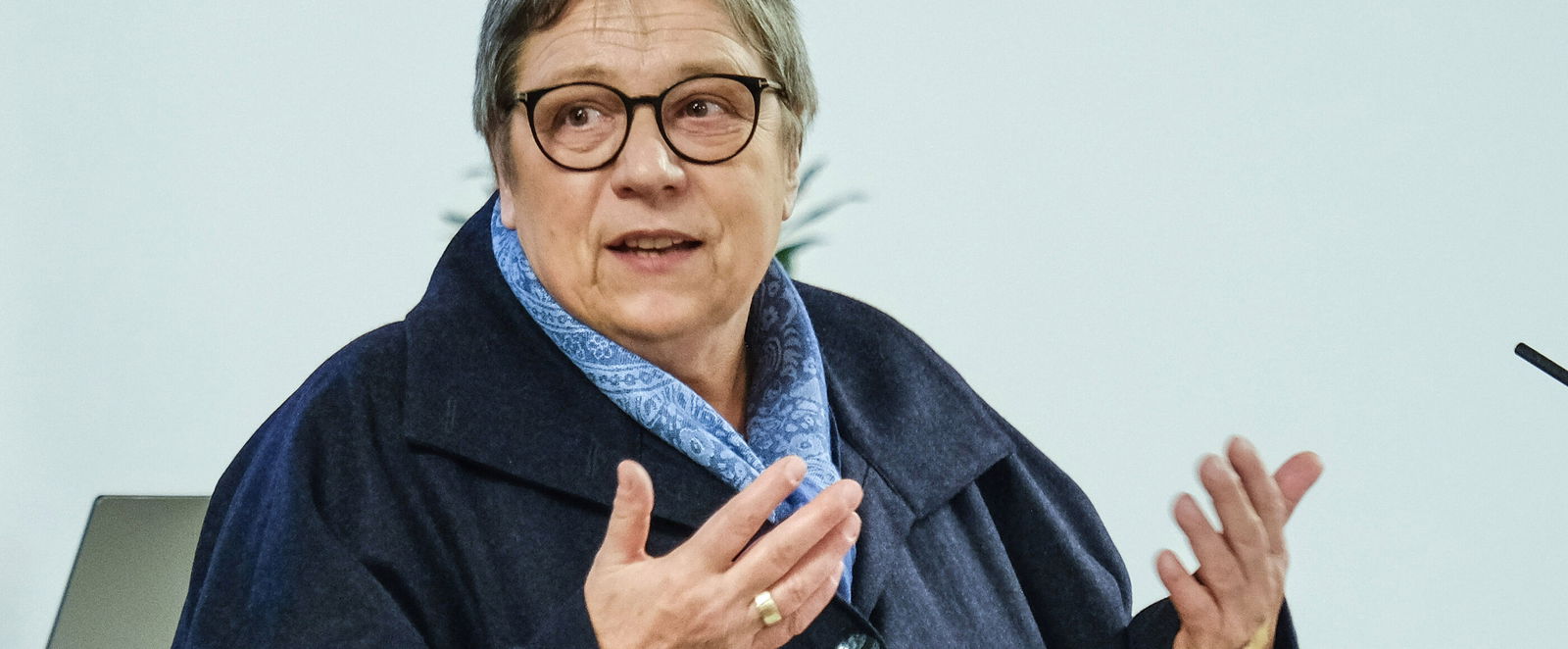 Eine weiblich lesbare Person steht an einem Pult und redet.