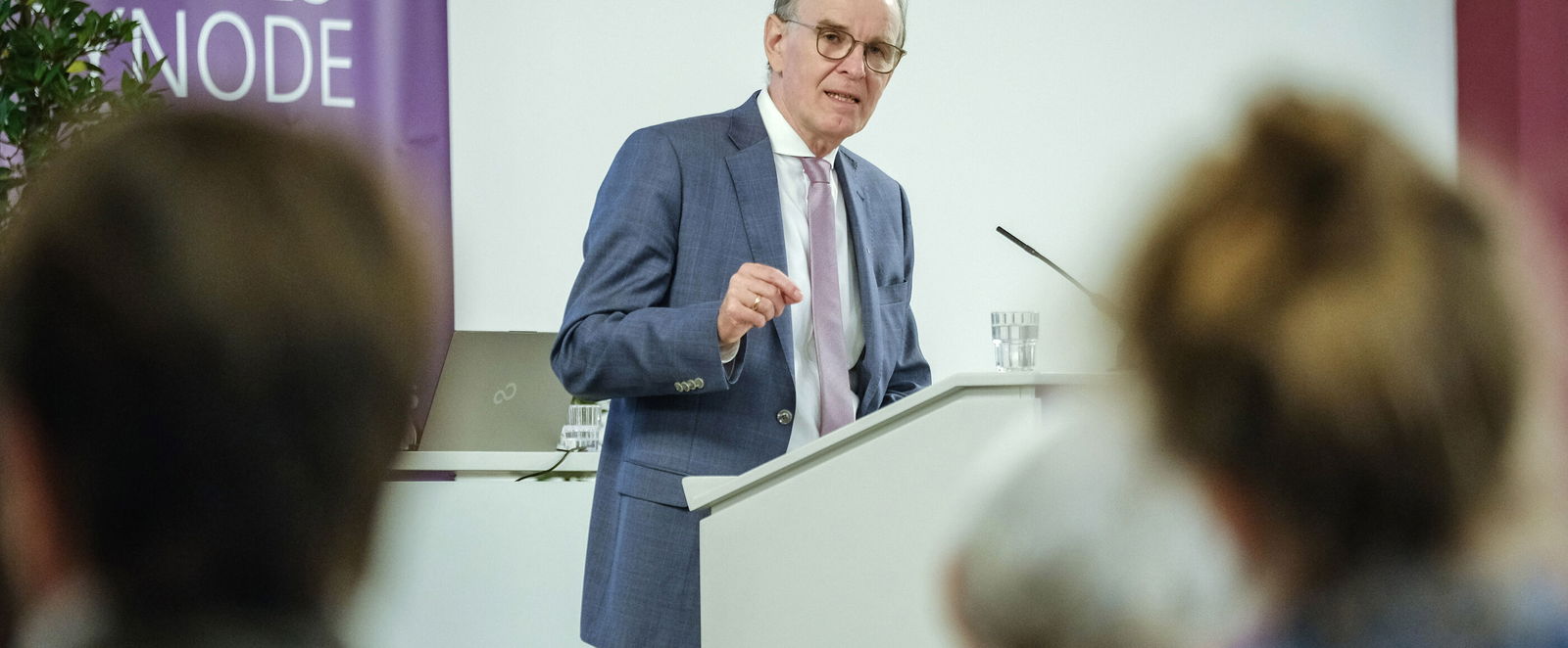 Eine männlich zu lesende Person an einem Redepult.