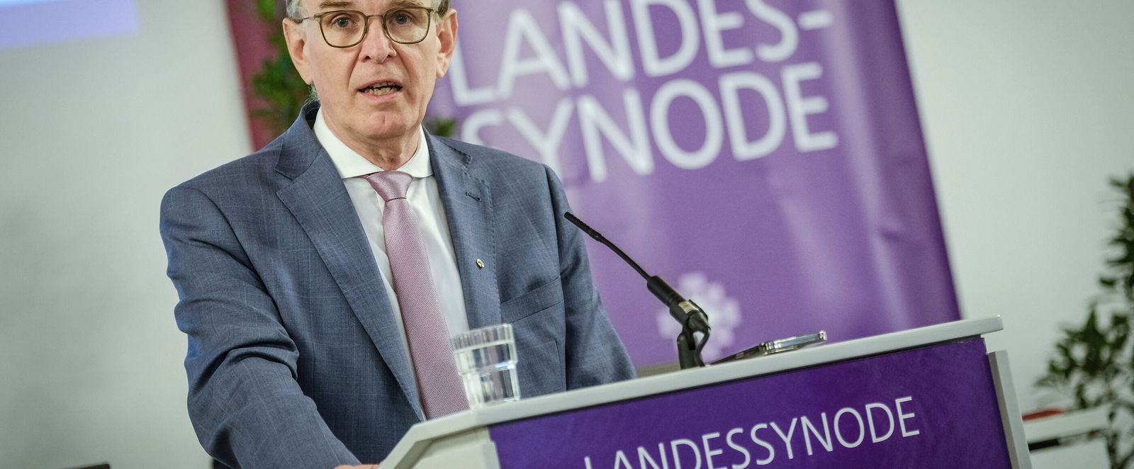 Eine männlich zu lesende Person steht an einem Redepult.