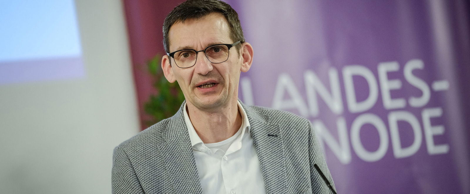 Eine männlich zu lesende Person spricht in ein Standmikrofon.