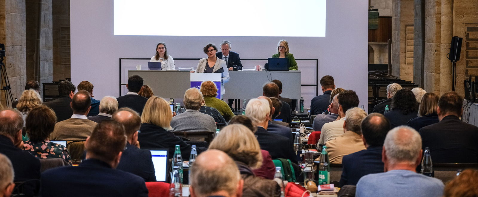 Mehrere Personen aus dem Plenum hören der vortragenden Person zu.
