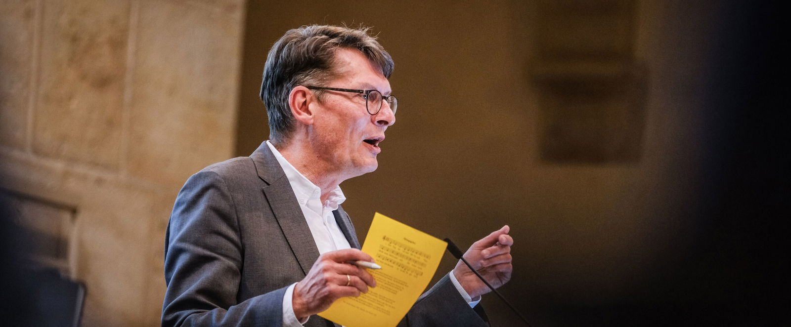 Eine männlich lesbare Person steht an einem Podium und spricht.