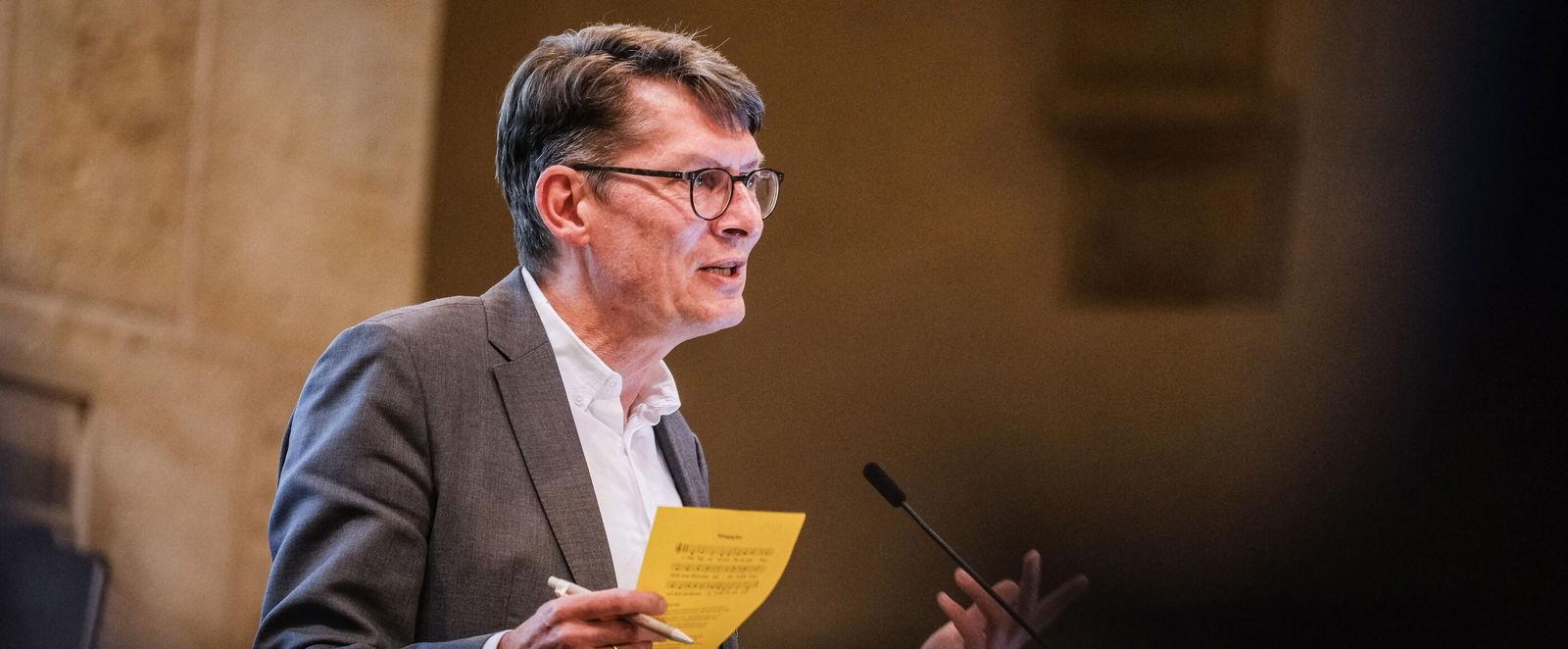 Eine männlich lesbare Person steht an einem Podium und spricht.