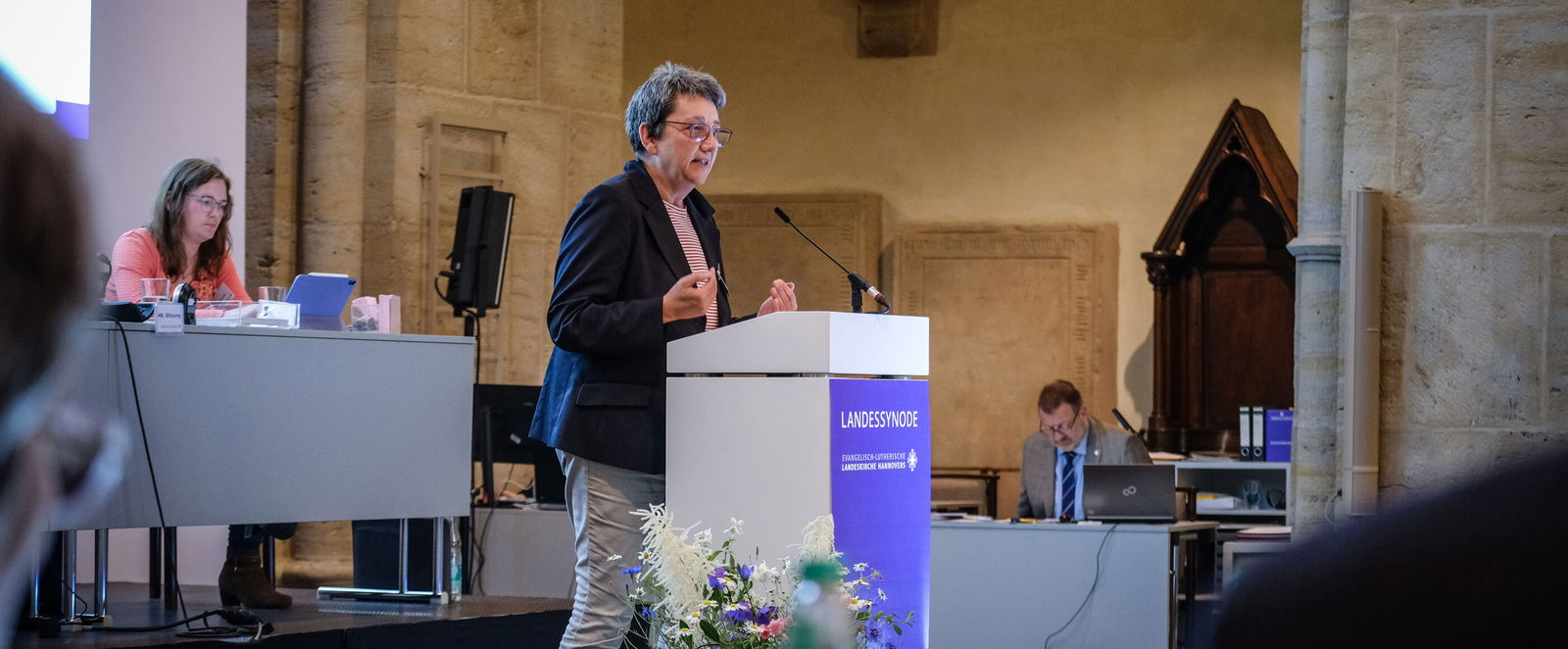 Eine weiblich gelesene Person steht vor einem Redepult.