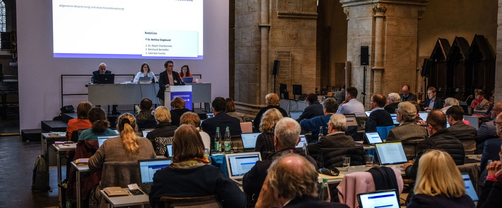 Mehrere Personen sitzen in einer zum Sitzungssaal umfunktionierten Kirche