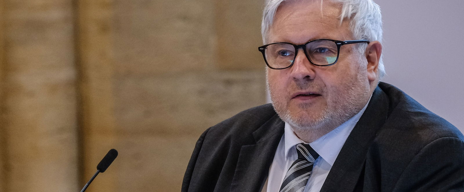 Eine männlich gelesene Person steht vor einem Redepult.