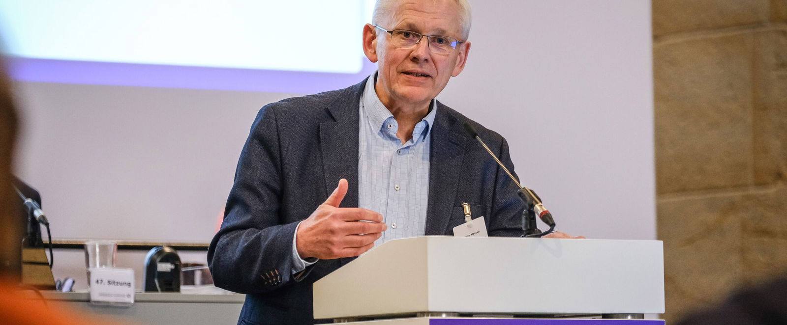 Eine männlich gelesene Person steht vor einem Redepult.