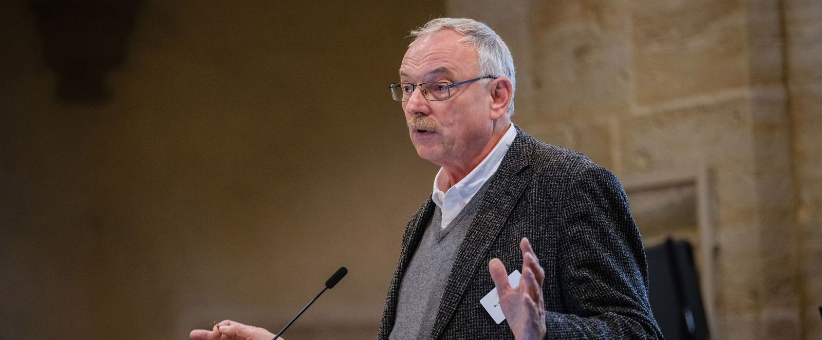 Eine männlich lesbare Person steht an einem Podium und spricht.