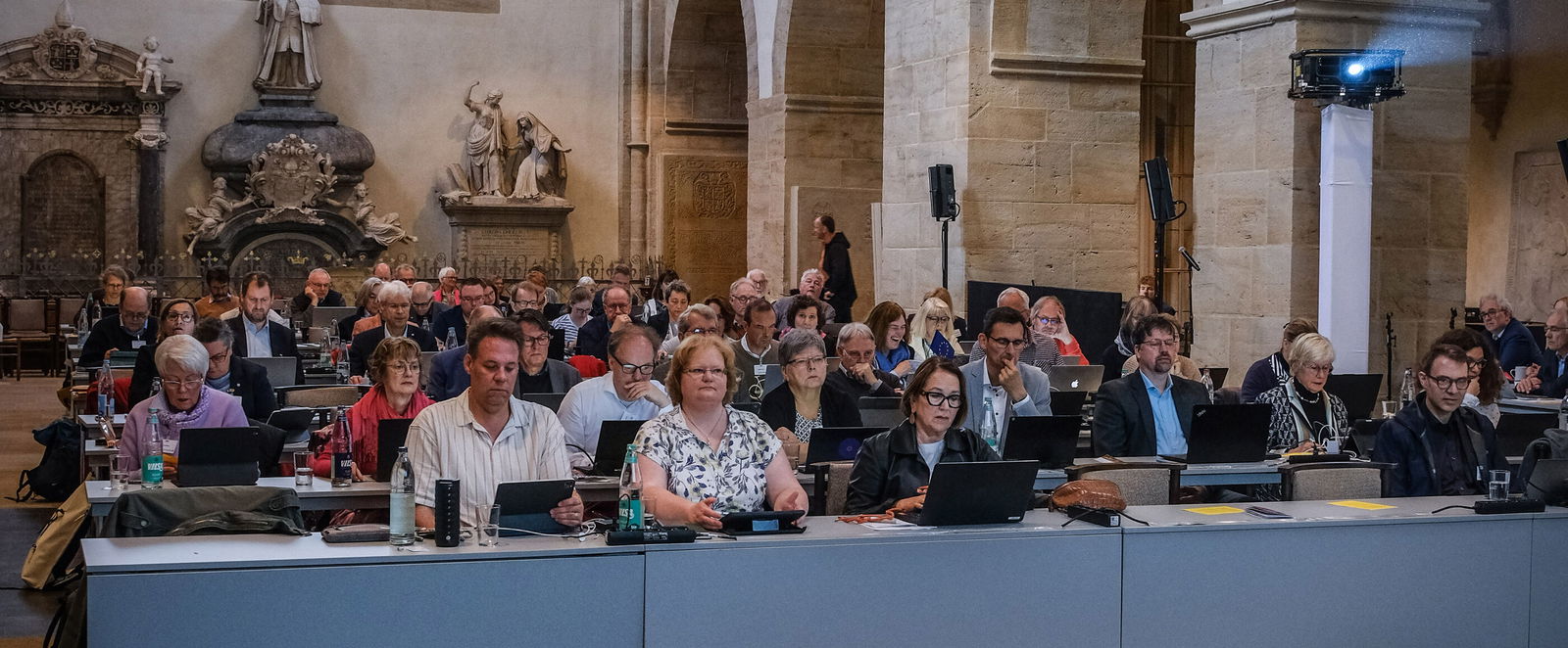 Mehrere Menschen sitzen in einer Kirche und hören der vortragenden Person zu.