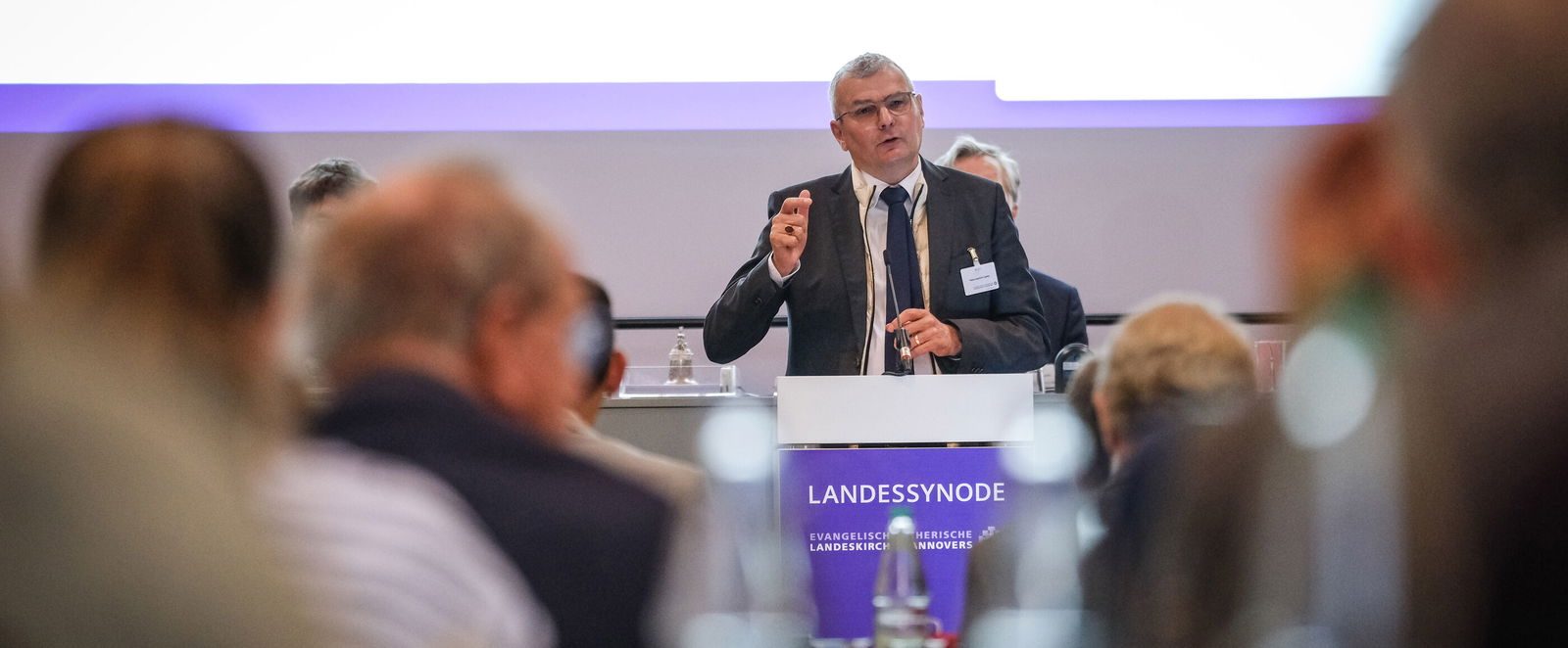 Eine männlich lesbare Person steht an einem Podium und spricht.