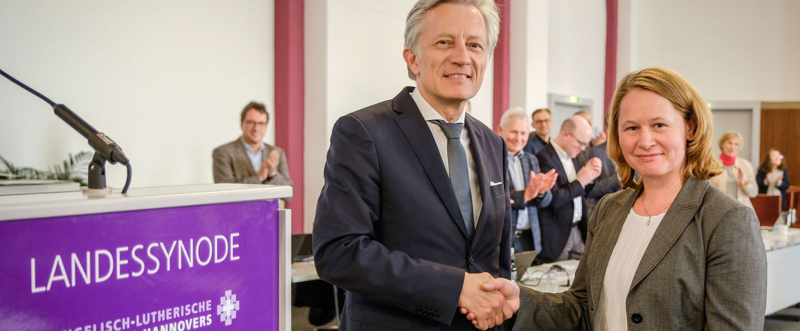 Eine als Mann und eine als Frau lesbare Person reichen sich die Hand.