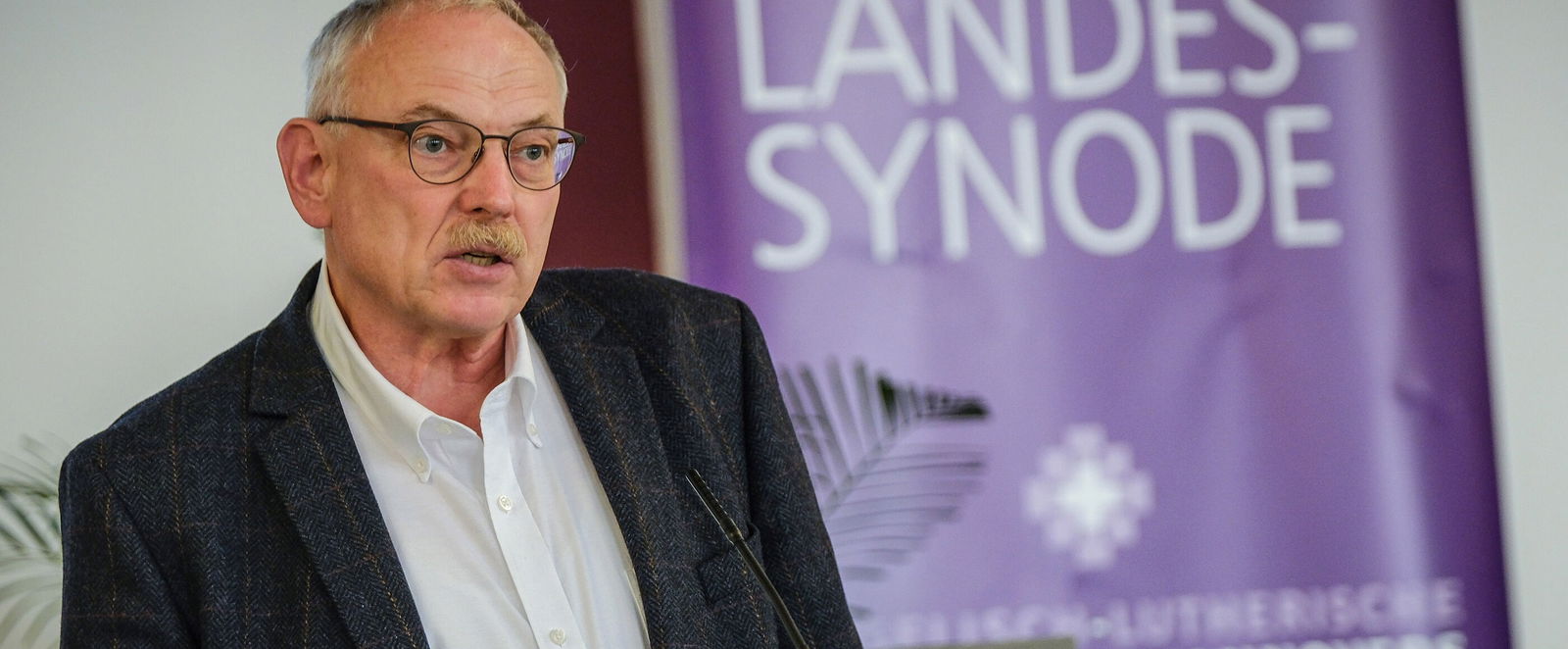 Eine männlich lesbare Person an einem Rednerpult