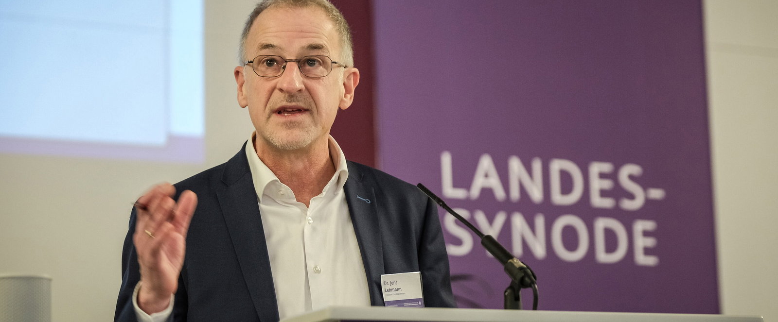 Eine als Mann lesbare Person mittleren Alters spricht an einem Redepult.